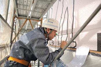 足場を組みヘルメットをかぶり作業服姿でビルの壁面に絵を描く若い男性