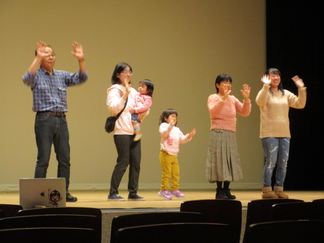 参加者が歌って踊る様子。小さなお子さんを抱っこしたお母さんもいます。