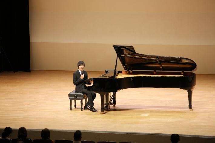 演奏者がピアノ椅子に座り観客席を向き詩を読んでいる