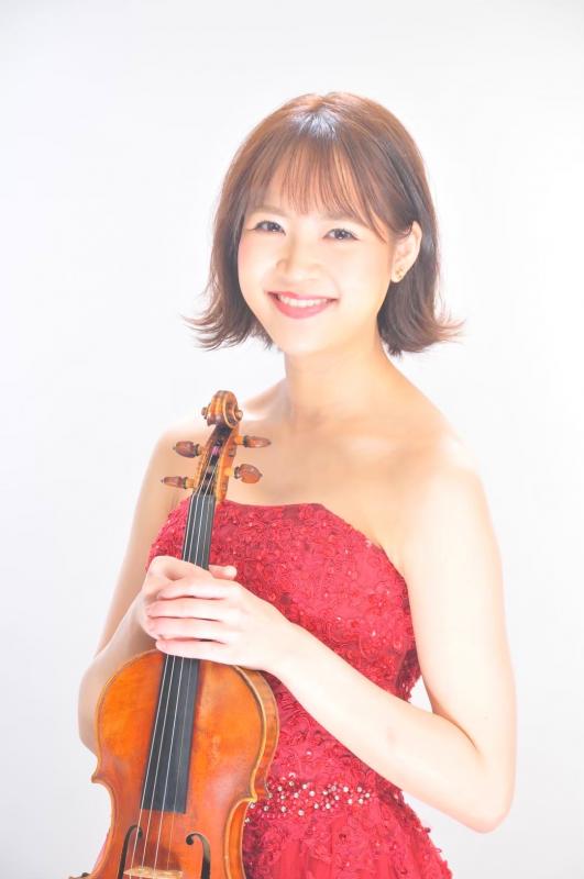 赤いドレスを着た女性がバイオリンを両手に持ち正面を向いている写真