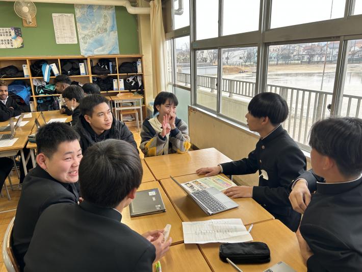 机に向かい合って交流をする外国出身者男女と中学生