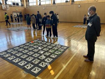 体育館に敷かれたシートの上で、ドローンを飛ばす子どもたち