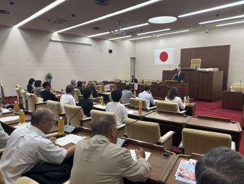 ひな壇型の席に着座する方々に向けてあいさつをする男性