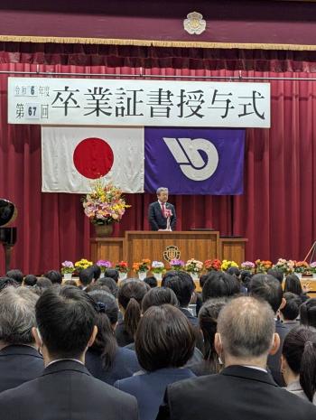 花で彩られた壇上からあいさつをする男性