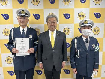 制服と帽子をまとう男性2名の中央に立つスーツの男性