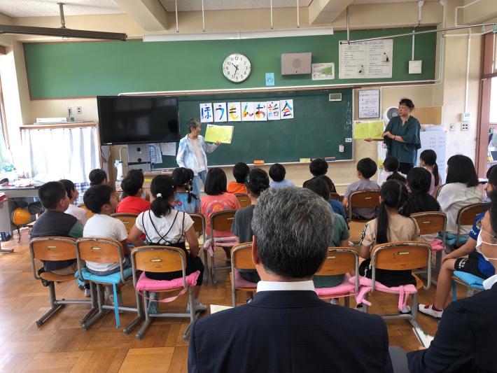 いすに座って絵本の読み聞かせを聞く子どもたち。読み聞かせは二人の女性が行っている。