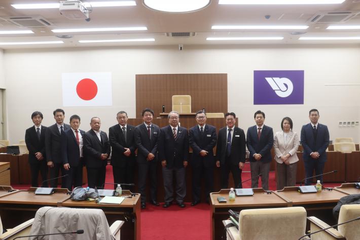 沖縄県うるま市議10名と取手市議2名が取手市議会議場で横一列に並んで記念撮影をしている様子
