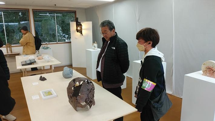 白い机の上に展示された作品を出展者と見る市長