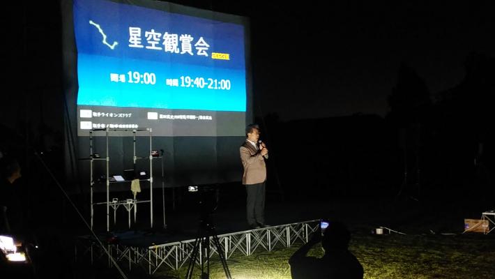 星空観賞会。「星空鑑賞会」という文字の浮かんだディスプレイの前にたち、マイクで何かを話している男性の写真。