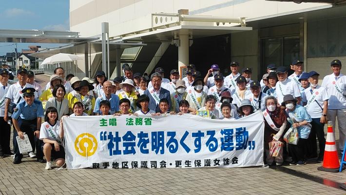 社会を明るくする運動参加者の集合写真。横断幕のうしろで幕を支えて並んで記念撮影している様子。