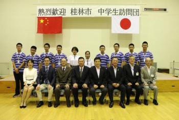 交流センターステージ前で、市長含む取手市幹部と桂林市側教育局の皆さんが前列に並び、後列に団員中学生が並んで撮影した記念写真画像。