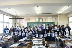 ユーバ市訪問団と学校の生徒が習字を持って集合写真に写っている様子