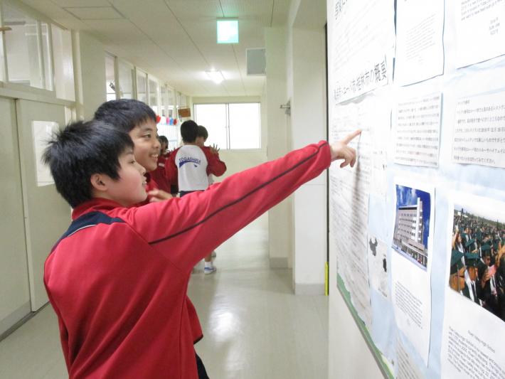 ユーバ市・桂林市の概要が書いてある模造紙を指さしながら見ている戸頭(とがしら)中学校の男子学生2名