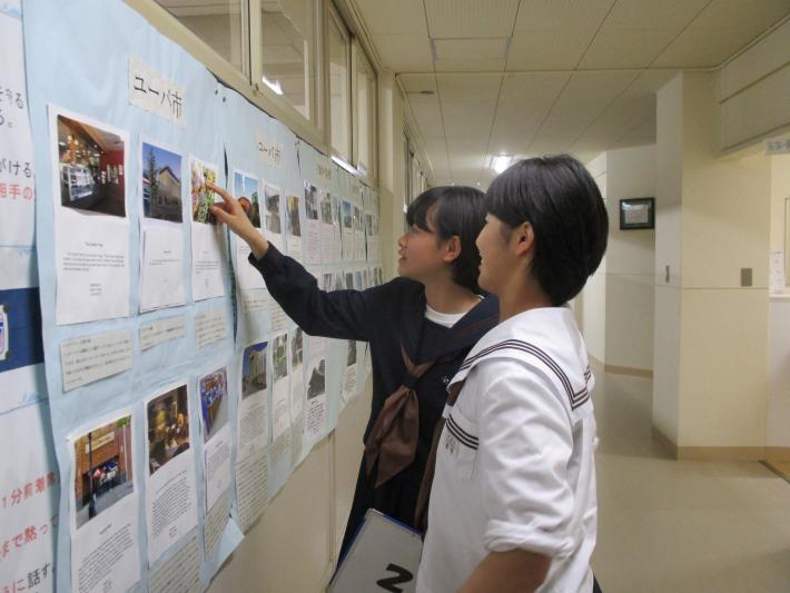 ユーバ市の学生による作品を指さしながら鑑賞する戸頭(とがしら)中学校の女子中学生2名