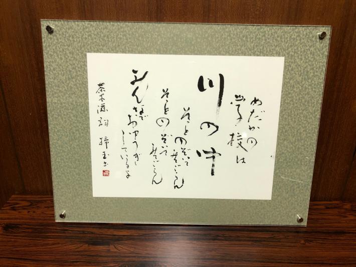 額に入った書の作品。童謡「めだかの学校」の歌詞が書かれている。