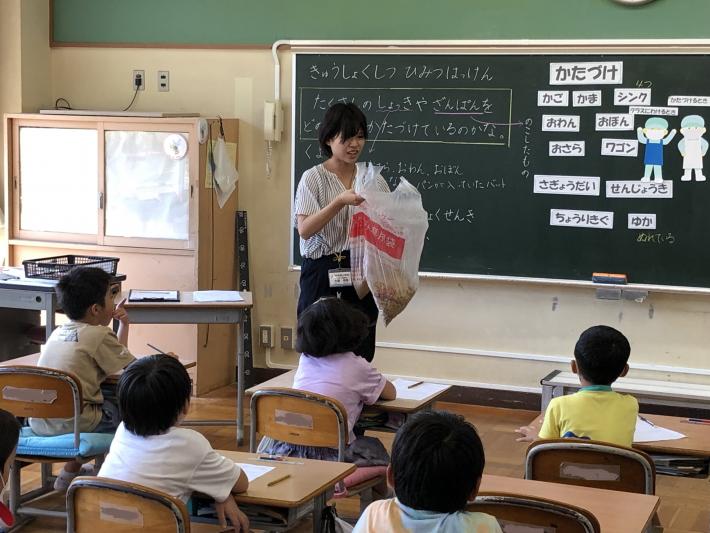 可燃ごみの袋に入った堆肥を子どもたちに見せる女性教諭