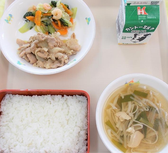 お盆にのせられた給食。赤く四角い入れ物に入ったご飯、牛乳、麺や野菜が入ったお椀、海老とチンゲンサイの炒め物と肉料理が白い皿に盛ら