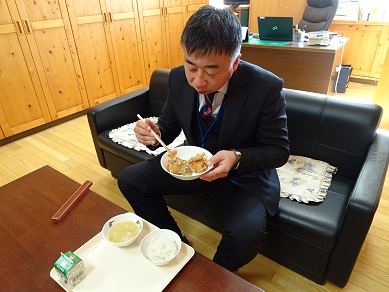 ソファーに座って給食を食べる大人