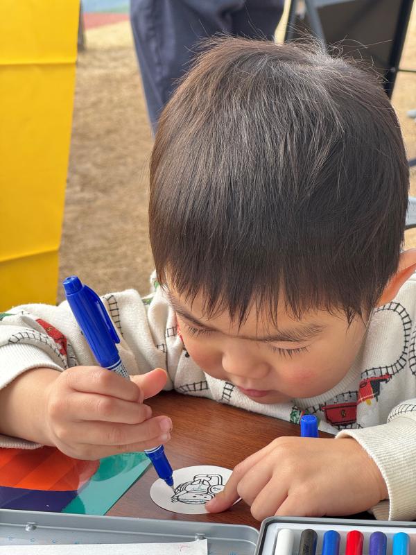 男の子が青いペンを持って丸い紙に絵を描いている