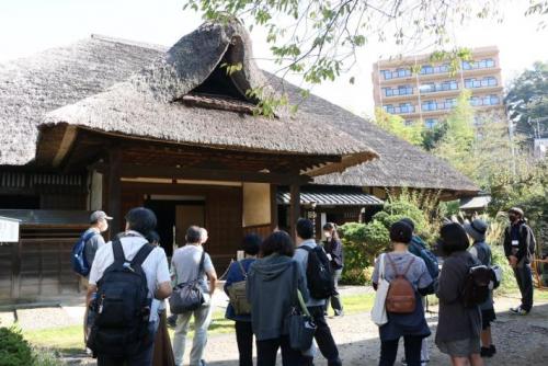 かやぶき屋根の本陣の建物の外に立って説明を聞く十数人の人々