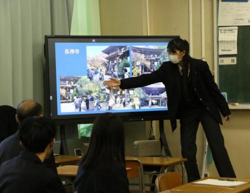 学生が画面を手で示しながら説明を行っている。他の学生がそれを聞いているようす