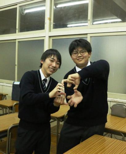 男子学生2人が手でよつばのようなマークをつくって笑顔で写真を撮っている