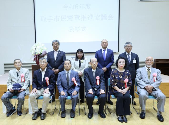 令和6年度の市民憲章推進協議会善行表彰式において写真に収まる受彰者6名と、間宮会長、中村市長、岩澤議長、石塚教育長